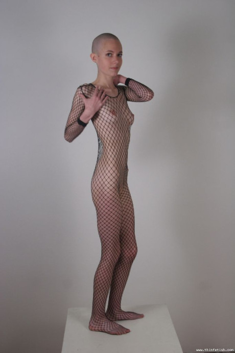 Solo model with a shaved head poses in a fishnet bodystocking