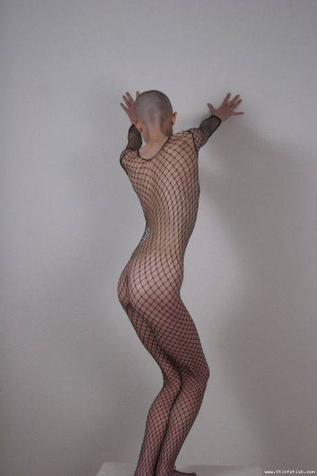 Solo model with a shaved head poses in a fishnet bodystocking
