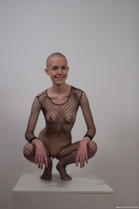 Solo model with a shaved head poses in a fishnet bodystocking