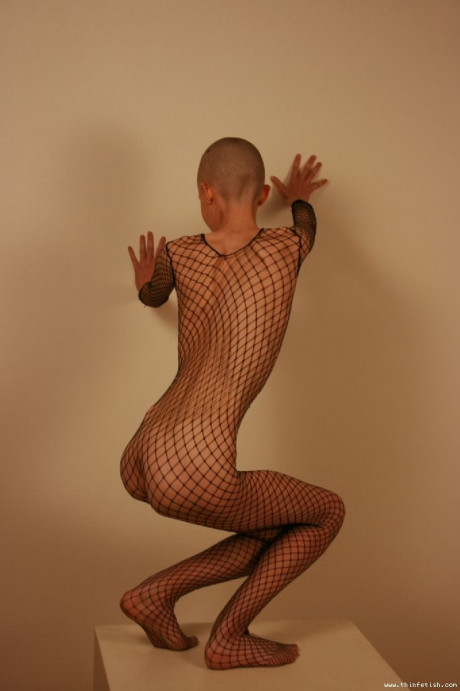 Solo model with a shaved head poses in a fishnet bodystocking