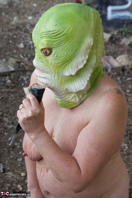 Undressed British lady chick Speedy Bee eats a fish while wearing a costume mask