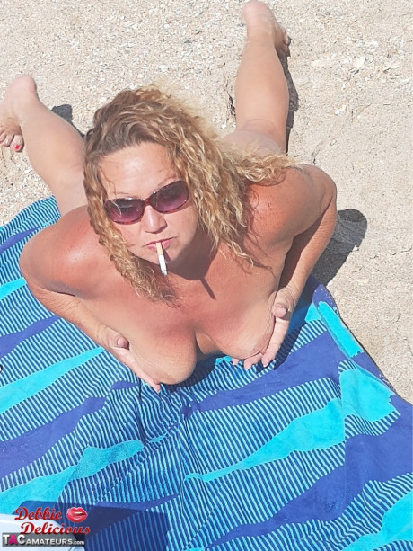 Older amateur Debbie delicious smokes while sunbathing in the naked on a beach