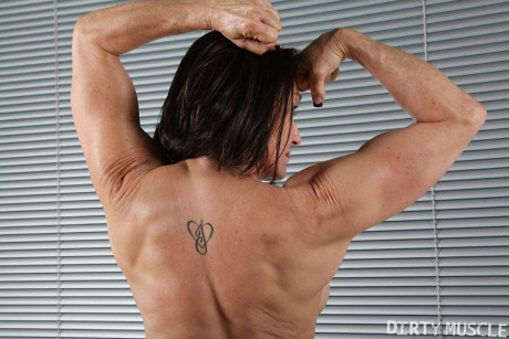 Female bodybuilder flexes after getting undressed on a mat in black socks